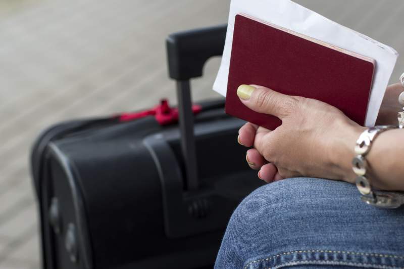 Black suitcase next to woman’s hands holding a small red booklet and papers.